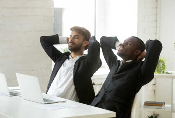 Two diverse businessmen relaxing after work breathing fresh air, relaxed african and caucasian partners in suits resting at workplace, executive corporate team enjoying break meditating in office